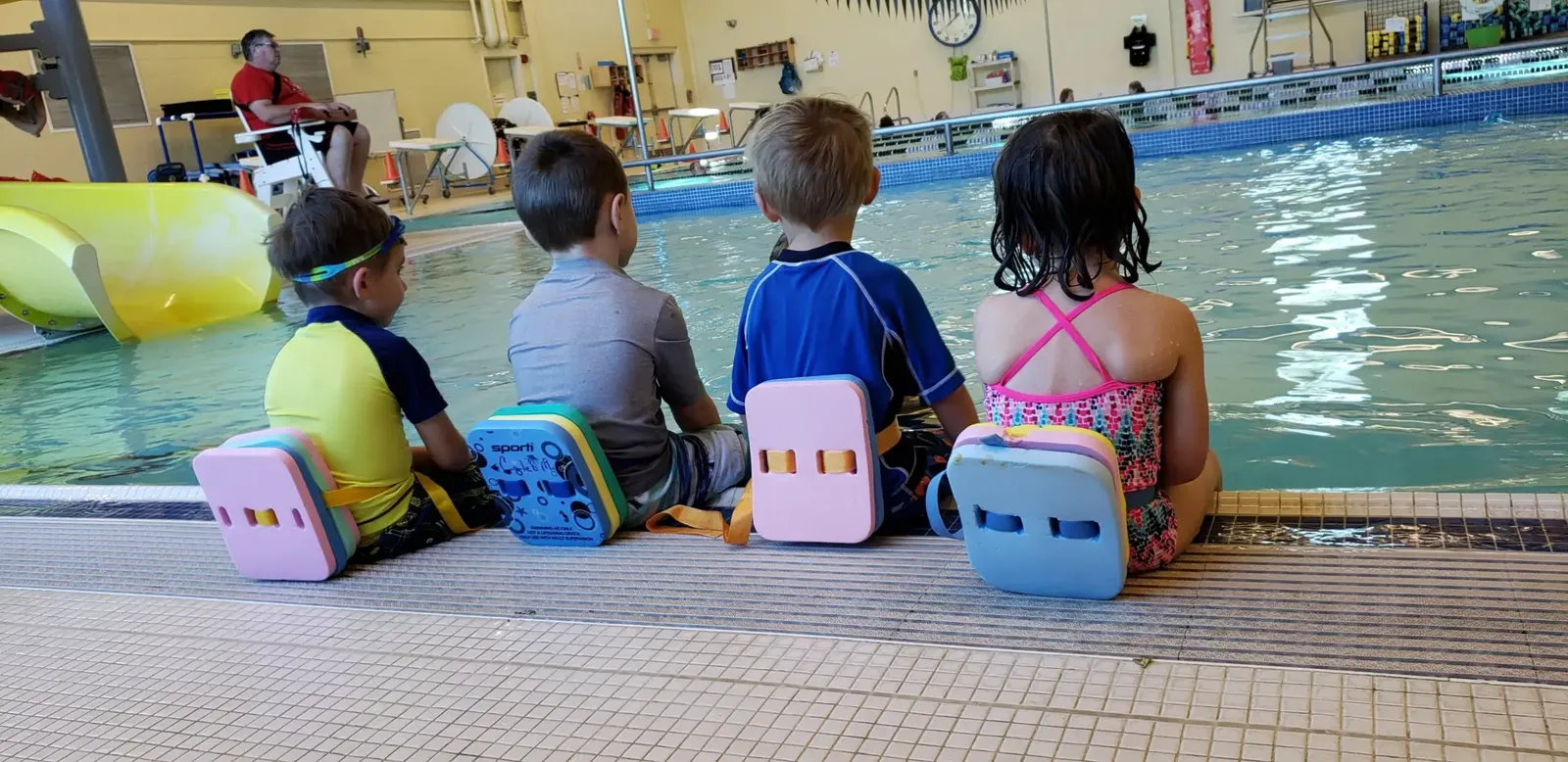 Young swimmers sitting at the edge of the pool during a swim lesson