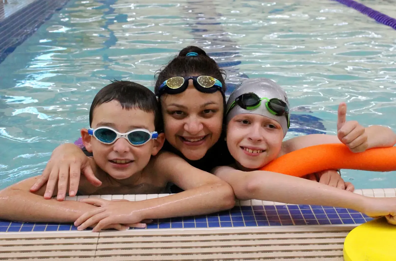 Swim instructor with two smiling kids in goggles at the pool wall