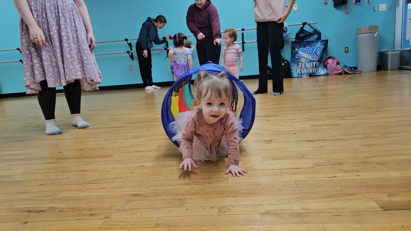 Toddler crawling through a play tunnel during a gym class